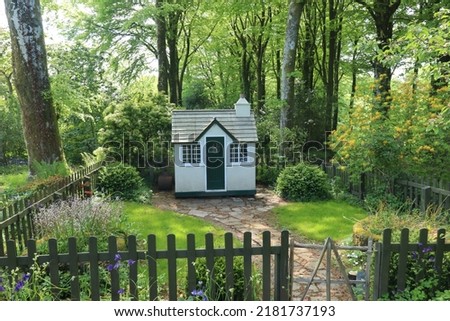 A small wooden children's play house in it's own little garden surrounded by a picket fence Royalty-Free Stock Photo #2181737193