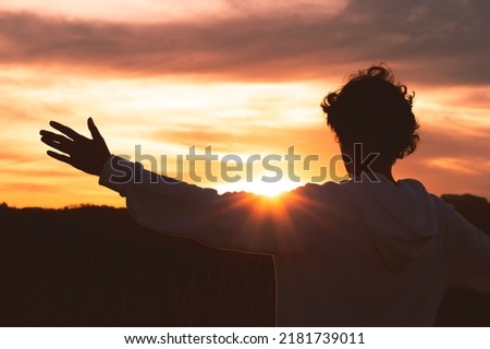 Silhouette of a man with arms raised and sunset in the background. Concept of happiness, mental health and well being. Royalty-Free Stock Photo #2181739011