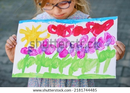 Little preschool girl holding picture painted with colorful water colors. Happy child with glasses, education and school concept. Creative leisure for children.