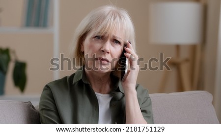 Caucasian old woman mature middle-aged 50s offended lady aged businesswoman sitting on sofa at home listening to voice on phone talking smartphone receiving bad news sadness worry upset losing failure Royalty-Free Stock Photo #2181751129