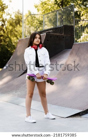 Child with penny board and headphones on skate playground. Young girl teenager with pennyboard stand on sport ramp. Extreme lifestyle. Creative advert for skate or penny board shops or stores