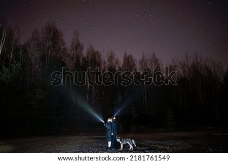 Romance, a man and a woman with flashlights hold hands under the starry sky, a husky stands nearby.  Photo with soft focus as an artistic technique.