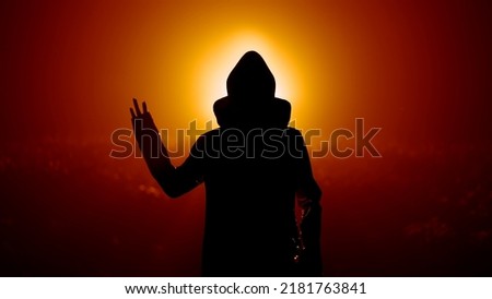 Silhouette of alien waving hand - hello on orange background. Humanoid on extraterrestrial planet. UFO, fantasy, futuristic, fiction concept. High quality photo