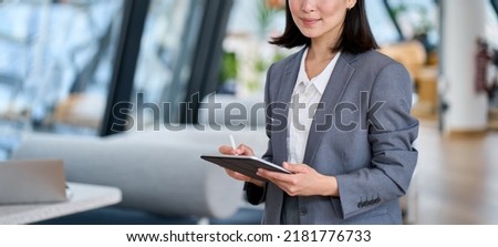 Smiling young Asian business woman leader holding digital tablet standing in office. Professional executive manager or saleswoman using corporate technology looking at camera. Portrait  Royalty-Free Stock Photo #2181776733
