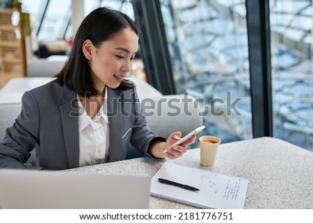 Young Asian business woman wearing suit working in modern office holding smartphone. Successful female chinese manager, professional worker using mobile corporate apps on cell phone at workplace. Royalty-Free Stock Photo #2181776751
