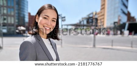 Young confident successful smiling Asian business woman entrepreneur wearing suit standing on city street advertising business trainings, corporate services, workshop, portrait. Banner with free space