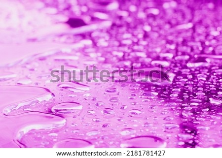Water drops on glass on blue and purple background. Bright blue water drop on glass, natural texture
