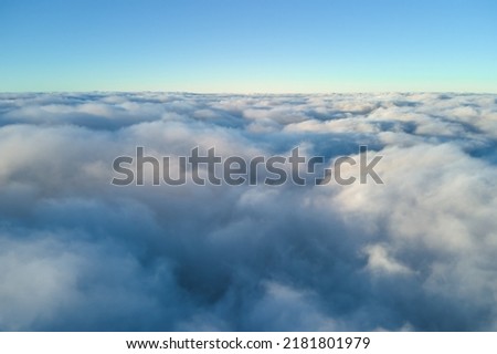 Aerial view from above at high altitude of dense puffy cumulus clouds flying in evening. Amazing sunset from airplane window point of view Royalty-Free Stock Photo #2181801979