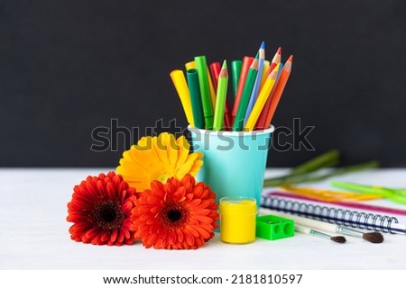 Time to return back to school. Bright colourful green yellow, blue stationery, paints, pencils, markers, brushes. black board on background. White alarm clock. Copy space for text. Autumn, September