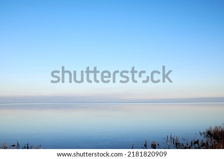 Sea at sunset with clear blue sky making a nature mirror reflection on the water with golden grey clouds on the horizon at dusk. Copy space, wallpaper background of beautiful and colorful ocean view Royalty-Free Stock Photo #2181820909