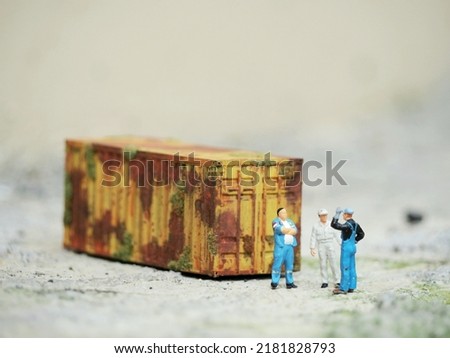 Miniature people and miniature container. Industrial concept photography. Many unfocus stuff at table. Conceptual design of toy photography.
