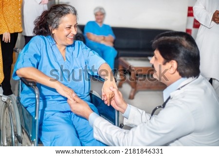 Indian doctor hold hand support and motivate disabled elder woman patient sit on wheelchair at home hospital, paralyzed old people healthcare concept. Royalty-Free Stock Photo #2181846331