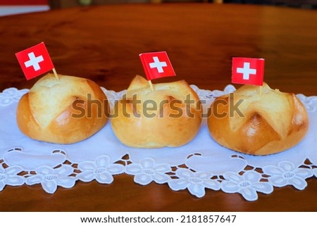 Traditional Swiss buns with a pattern in the shape of the Swiss flag is baked on the eve of the Swiss National Day on August 1st. Buns lie on a wooden table covered with a napkin with the embroidery.
