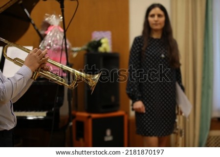 A student playing a golden trumpet in a classroom in class with a female teacher a young brunette with long hair watching a practice focus on a musical instrument close up Royalty-Free Stock Photo #2181870197