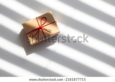 Top view on small brown gift box tied with red cord on white background with diagonal stripes and shadows
