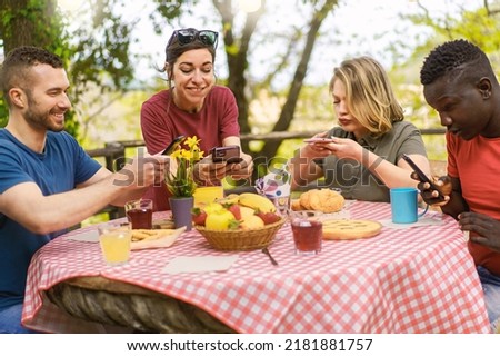 Group of multiethnic friends having fun taking pictures of food sitting at picnic table - food blogger and influencers wannabe concept