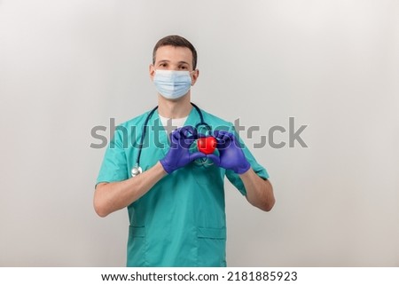 Male cardiologist  in a mask and gloves with stethoscope  with heart. Doctor is holding a red heart. Heart healthcare concept. Copy space.