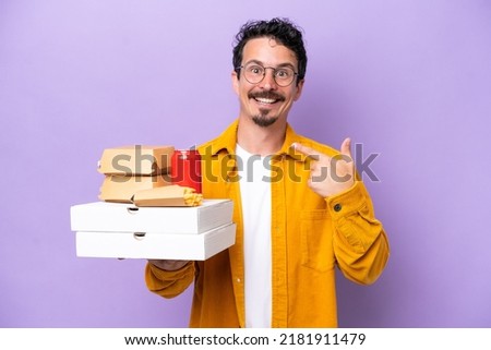 Young caucasian man holding fast food isolated on purple background giving a thumbs up gesture