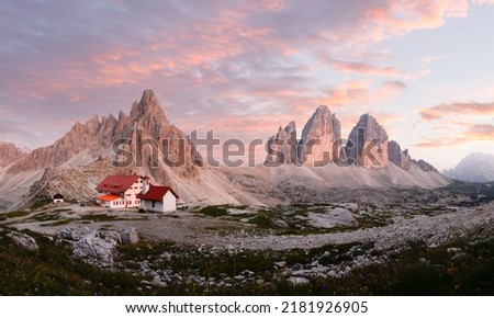 Stunning panoramic view of the Three Peaks of Lavaredo, (Tre cime di Lavaredo) Mount Paterno and a refuge during a beautiful sunset. Royalty-Free Stock Photo #2181926905