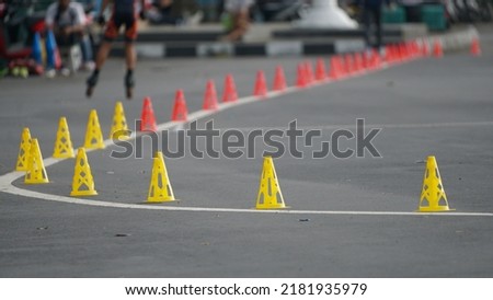 Plastic orange slalom cones line up on asphalt ground outdoors. Skater is on a blurred background. Selective focus.