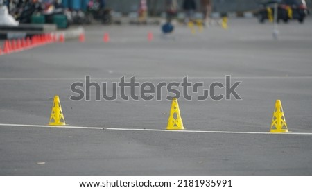 Plastic orange slalom cones line up on asphalt ground outdoors. Skater is on a blurred background. Selective focus.