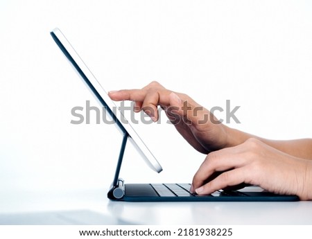 Person's finger touching, drawing on digital tablet screen while typing on keyboard computer with another hand isolated on white background with copy space, side view. Work with technology.