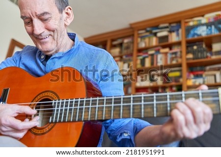 Smiling elderly man playing classical guitar with library on background Royalty-Free Stock Photo #2181951991