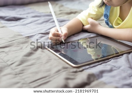 Beautiful asian child girl portrait using tablet computer drawing cartoon lying on bed