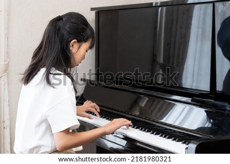 Japanese girl playing upright piano Royalty-Free Stock Photo #2181980321