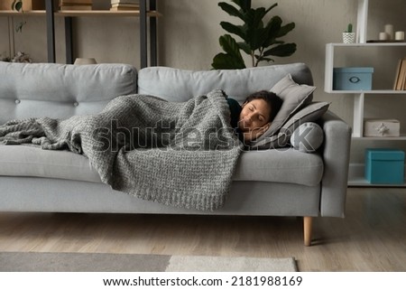 Full length peaceful woman resting under warm blanket on cozy couch in living room, calm young female with closed eyes sleeping, taking nap or daydreaming, lying on soft pillow with hands under cheek Royalty-Free Stock Photo #2181988169