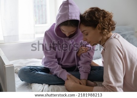 Caring mother hugging, comforting depressed upset teenage daughter, stressed unhappy teenager girl wearing hood sitting on bed, thinking about problems, feeling lonely and misunderstood Royalty-Free Stock Photo #2181988213