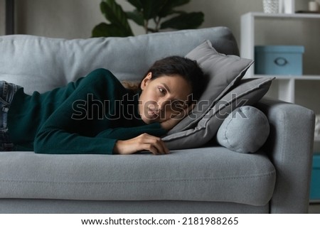 Close up frustrated woman lying on couch alone, feeling depressed and lonely, thinking about relationships or personal problems, hopeless young female lost in thoughts, suffering from break up Royalty-Free Stock Photo #2181988265