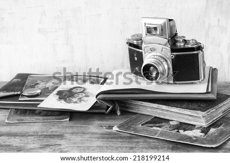 vintage camera, antique photographs and books over wooden table. black and white photo.