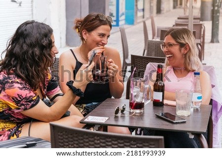 A group of four friends meeting up again during the summer holidays. Two of them laughing, another with her mobile phone and the fourth taking the photo.
