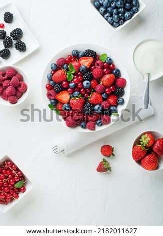 Bowl of healthy fresh berry fruit salad with cream on white background. Top view. Berries overhead closeup colorful assorted mix of strawberry, blueberry, raspberry, blackberry, red currant Royalty-Free Stock Photo #2182011627