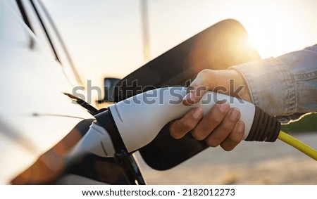 woman hand charging a electric car at the electric gas station with sunlight Royalty-Free Stock Photo #2182012273