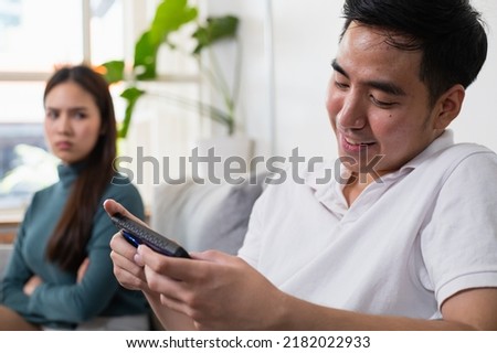 Young Asian couple in which the man plays the game and ignores his wife. His wife's face was filled with indignation. Royalty-Free Stock Photo #2182022933