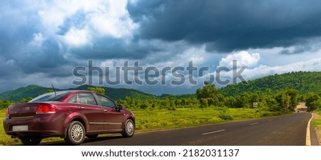 A Red Sedan Parking on the Roadside Overlooking Mountains with moody skies . Selective Focus is used.  Royalty-Free Stock Photo #2182031137