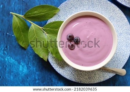 Bowl with yogurt close up photo. Non-dairy blueberry yogurt on a table. Healthy eating concept.  Blue textured background with copy space. 