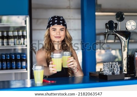 Hipster girl bartender serving fresh lemonade behind counter at outdoor bar during summer festival Royalty-Free Stock Photo #2182063547