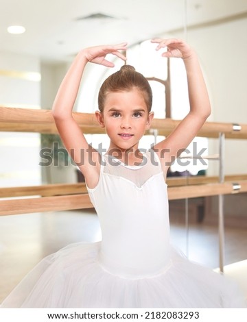 cute little ballerina standing with her hands up in a performance dress. She is dreaming to become a professional ballet dancer. Dance school, ballet studio.