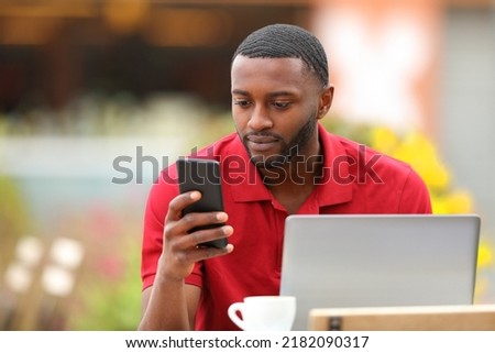 Black man in red using phone and laptop in a coffee shop terrace Royalty-Free Stock Photo #2182090317
