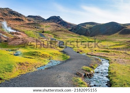 Pathway by stream flowing in mountain. Beautiful view of amidst green moss covered landscape against blue sky. Idyllic picturesque of volcanic valley in Alpine region. Royalty-Free Stock Photo #2182095155
