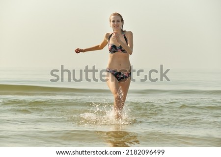 single happy young blond hair woman in bikini running at sea surf with splashes