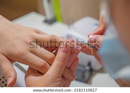 Manicurist master removing cuticles. Processing of rough cuticles and lateral folds of nails on hands with a conical instrument. Medical hardware manicure in a beauty salon Royalty-Free Stock Photo #2182110827