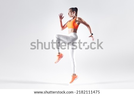 Attractive young woman in sports clothing jumping against white background