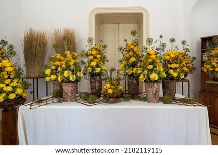 lots of yellow roses in different wooden ( cork ) vases, bouquet of roses with poppy heads in a room on table in a historical building, wedding decoration concept