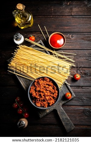 Bolognese sauce in a bowl on a cutting board with spaghetti dry. On a wooden background. High quality photo