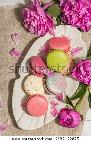 Macarons with a bouquet of peonies on white wooden background. Sweet dessert, colorful and pastel colors, summer concept. Romantic rustic style, festive card, hard light, dark shadow, top view