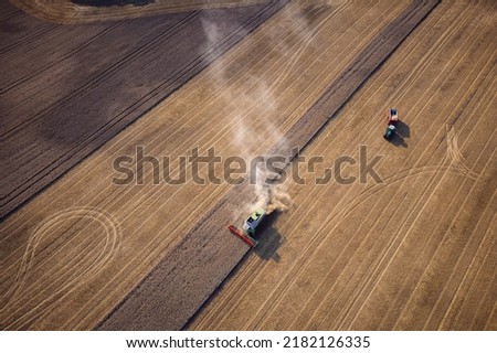 Agricultural machines harvest wheat in the field. Aerial shot from above. There is a lot of dust around the harvester.